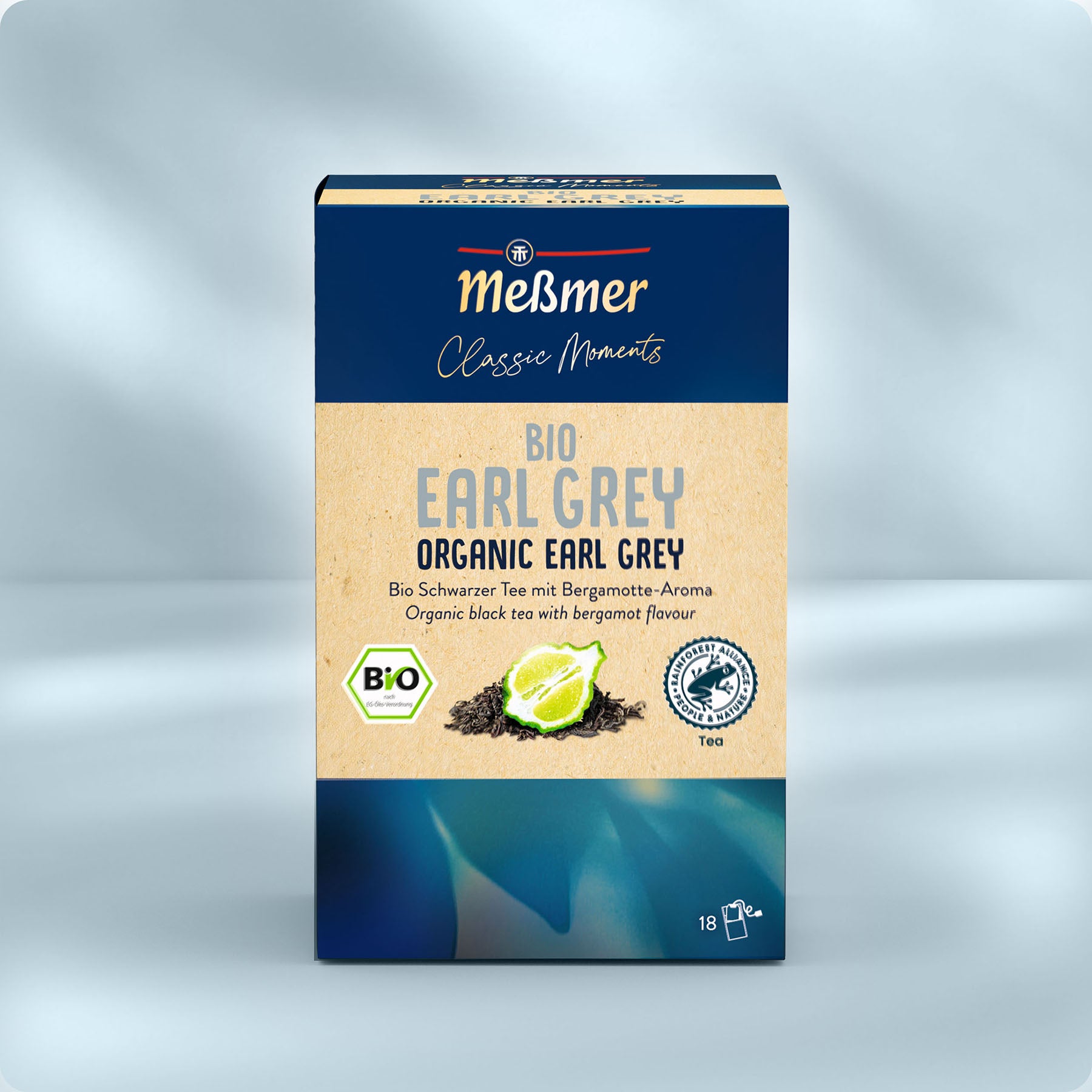 Eine Schachtel Meßmer DE Bio Earl Grey mit losen Teeblättern und einer Zitronenscheibe auf einer blau-beigen Verpackung mit deutsch-englischem Text, die durch ihr unverwechselbares Bergamotte-Aroma besticht.