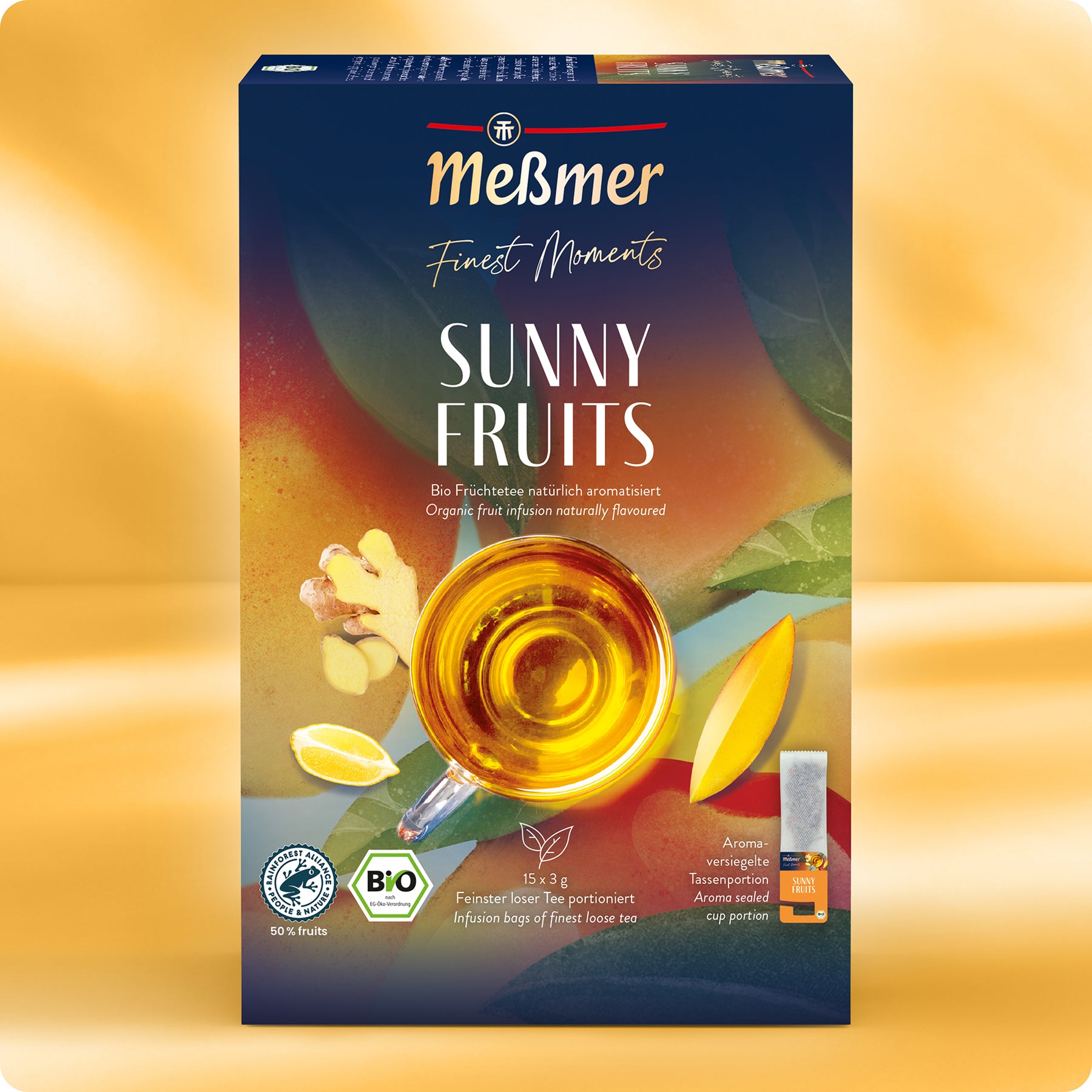 Eine Schachtel Meßmer DE Bio Sunny Fruits zeigt eine Glastasse mit Tee, Beeren- und Ingwergrafiken sowie Bio-Etiketten auf einem gelb-orangen Farbverlauf. Die Früchtetee-Packung enthält 15 Aufgussbeutel.