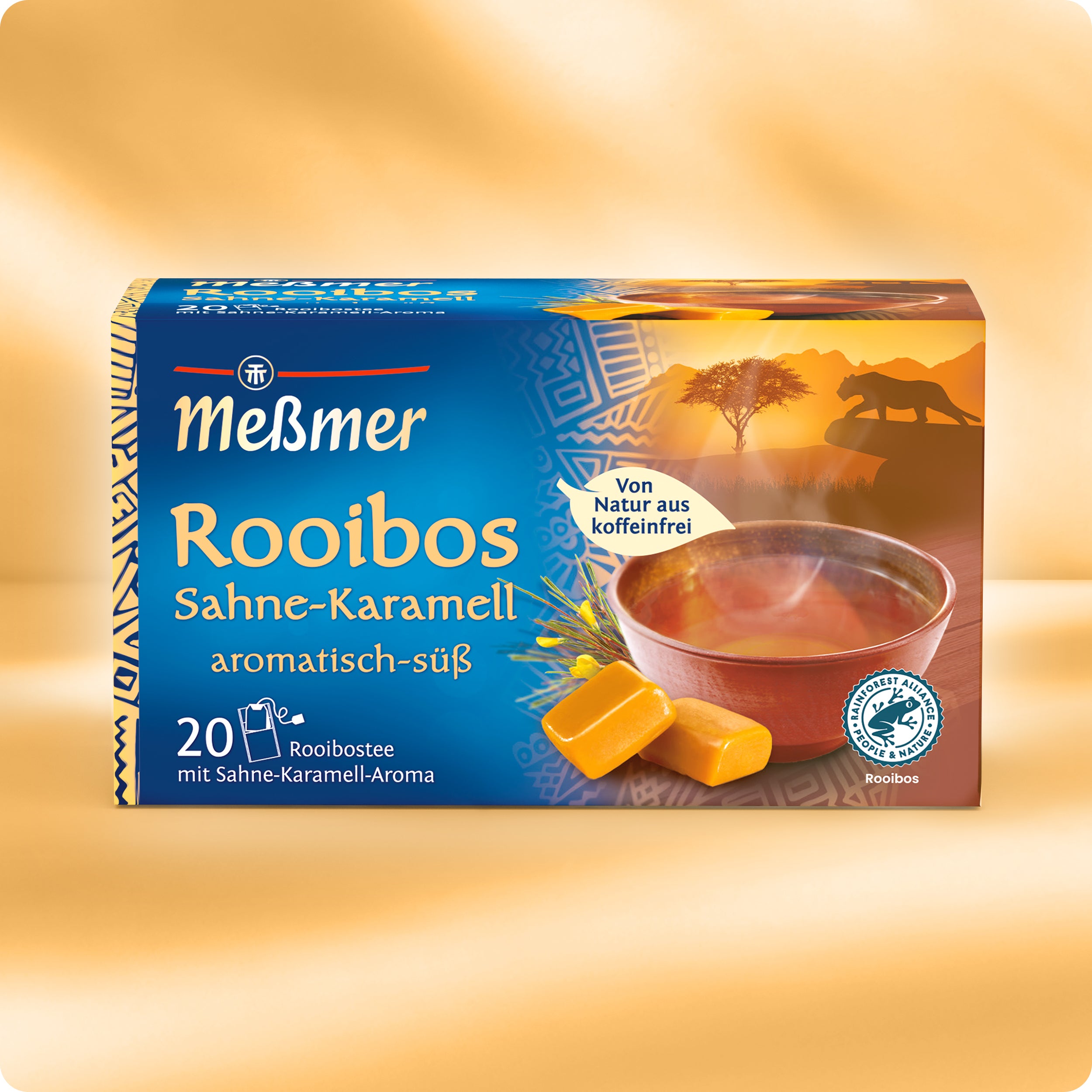 Eine farbenfrohe Schachtel Meßmer DE Rooibos Sahne-Karamell-Tee mit einer Tasse koffeinfreiem Tee, Karamellstückchen und einer afrikanischen Savannenszene mit Elefant und Akazienbaum. Enthält 20 Teebeutel.