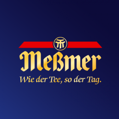 Logo der Teemarke Meßmer auf dunkelblauem Hintergrund. Das Logo zeigt Meßmer in Gold, stilisierten deutschen Text, eine rote horizontale Linie mit einem runden Emblem darüber und den Slogan Wie der Tee, so der Tag. in Gold darunter.