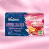 Verpackung von Himmelszauber Winterpunsch-Mandel Früchtetee mit dampfender Teetasse, Aprikosen, Mandeln und Hinweis auf fruchtig-würziges Aroma vor winterlichem rosa Hintergrund.