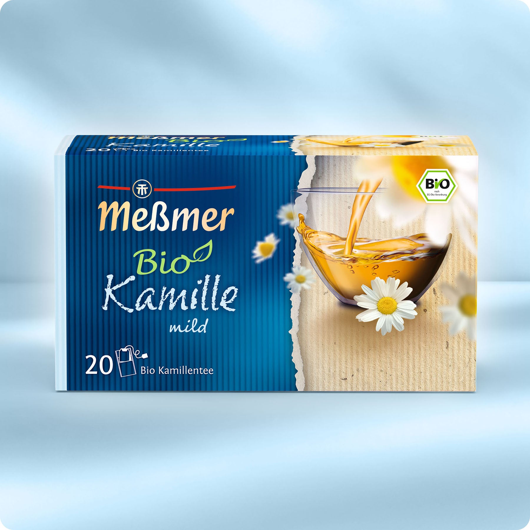 Eine Schachtel Meßmer DE Bio Kamille Tee mit 20 Beuteln zeigt ein blau-beiges Design, Kamillenblüten, ein Glas Tee und ein Bio-Etikett.