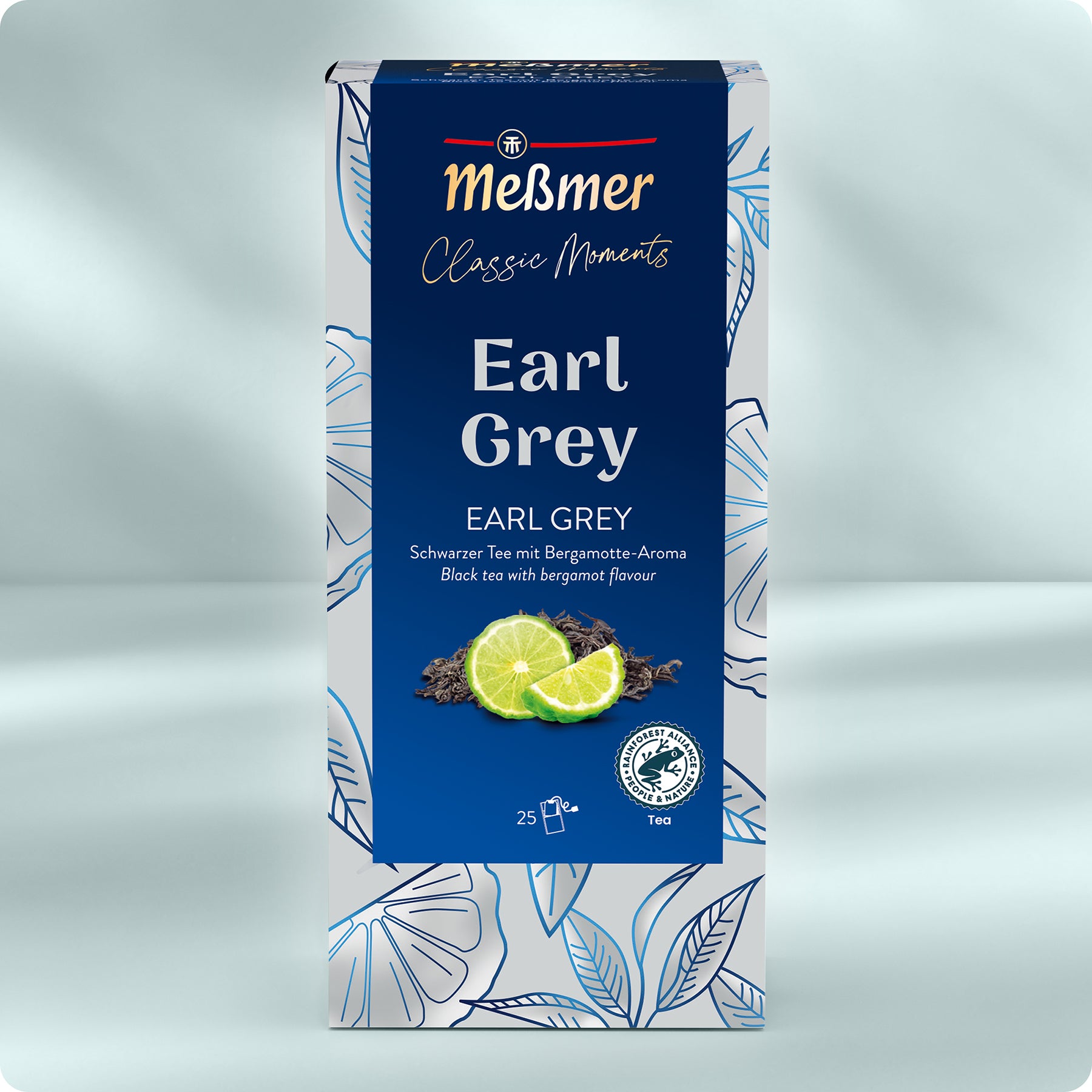 Eine Schachtel Meßmer DE Earl Grey Tee, verziert mit weißen und blauen Blättern. Die Vorderseite zeigt losen Tee, zwei Limettenscheiben und einen zweisprachigen Text. Diese Mischung mit Bergamotte-Geschmack enthält 25 Teebeutel.