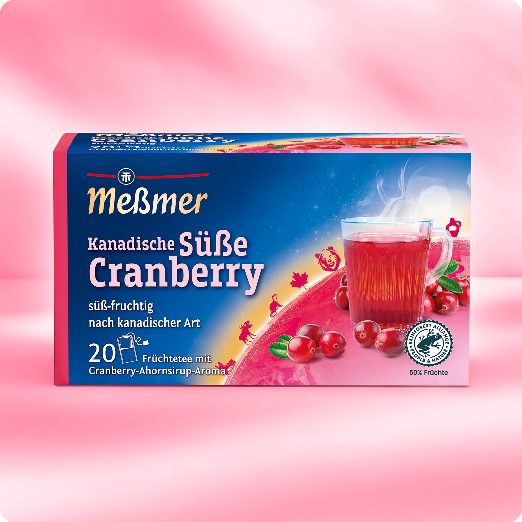 Eine Schachtel Meßmer DE Kanadische Süße Cranberry-Tee steht auf einer rosafarbenen Fläche mit einem Glas rotem Cranberry-Tee, kanadischen Cranberries und Cranberry-Blättern; die Verpackung enthält Produktinfos und fruchtige Bilder für ein fruchtiges Aroma.