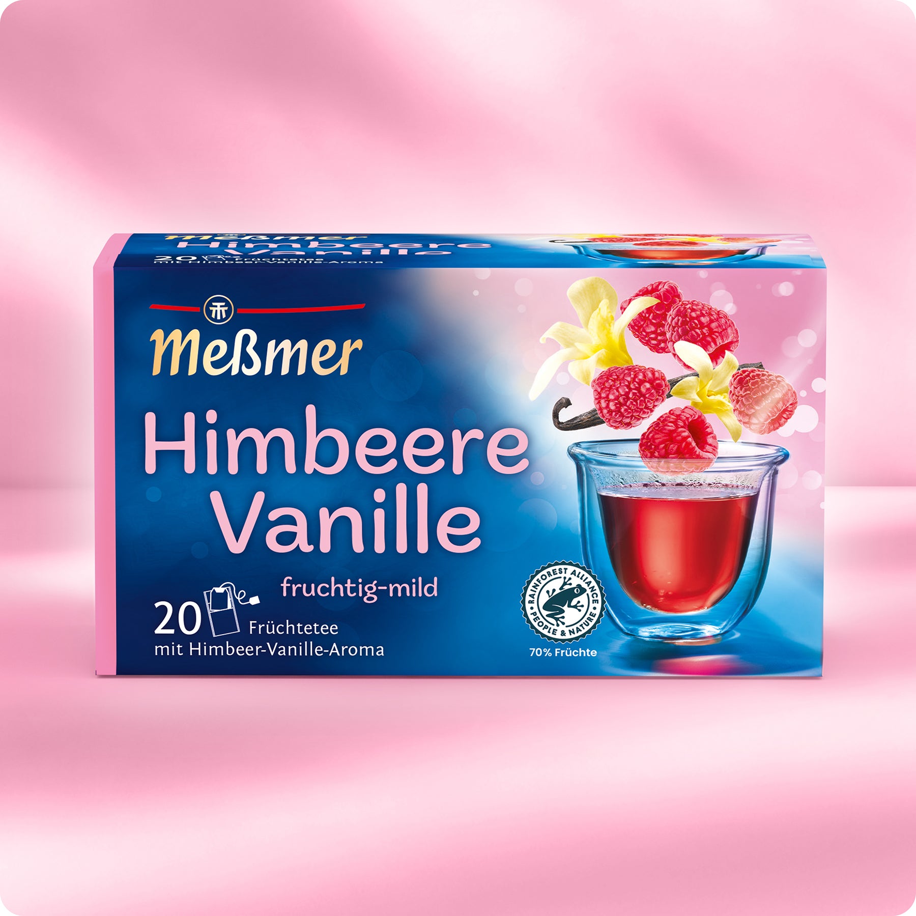 Eine Schachtel Meßmer DE Himbeere Vanille Tee steht auf einer rosafarbenen Verpackung, die ein Glas mit rotem Tee, Himbeeren, Vanilleblüten und -schoten zeigt, sowie einen Text, der 20 Teebeutel und 70% Fruchtgehalt mit feinen Vanillenoten hervorhebt.