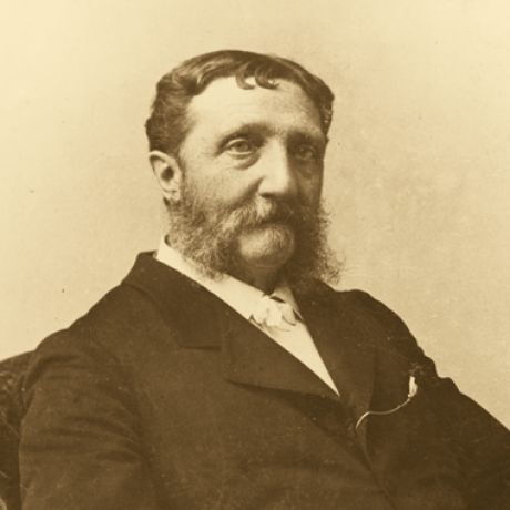 Sepiafarbenes Porträt eines Mannes mittleren Alters mit kurzem, gewelltem Haar, ausgeprägten Koteletten und einem Schnurrbart. Er trägt einen dunklen Anzug und ein helles Hemd und blickt leicht zur Seite mit einem neutralen Ausdruck.